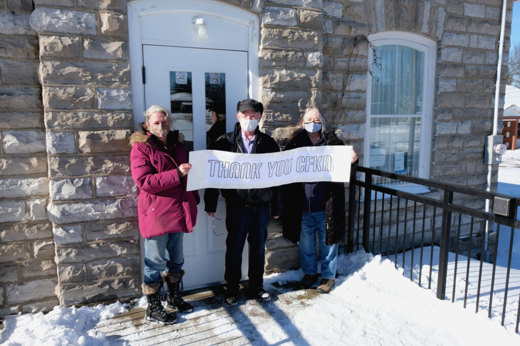 Three museum members holding a thank you sign outside the museum in the winter
