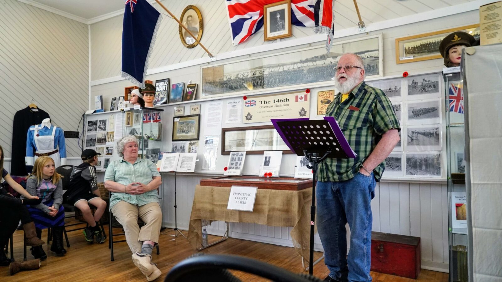 Two elderly men in a room filled with framed memorabilia and flags.