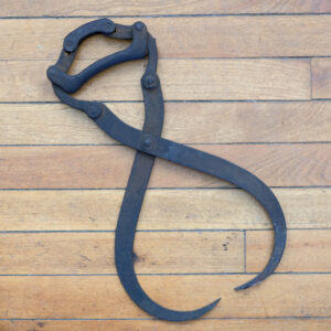 Vintage log grapple tool on wooden floor.