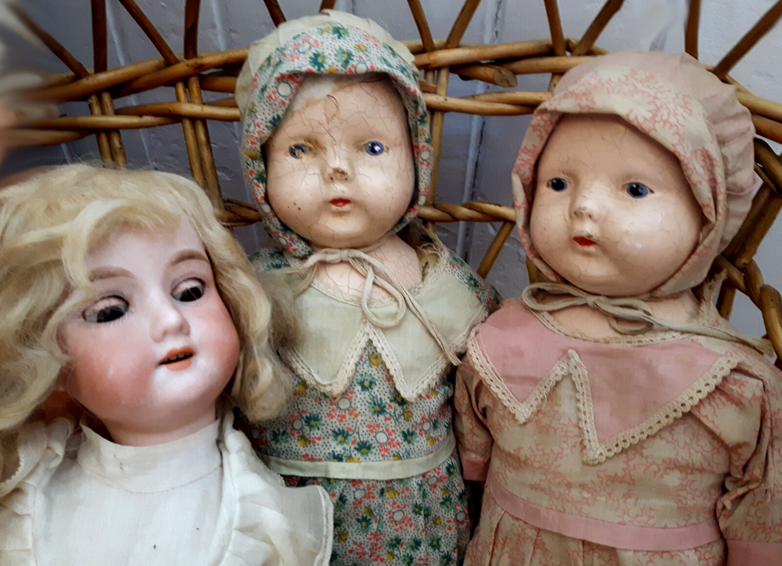Three vintage dolls with bonnets and dresses.
